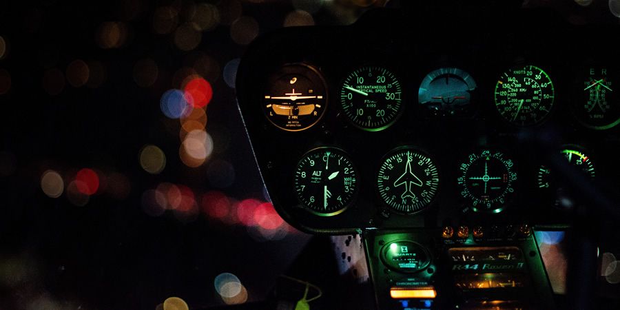 A lit helicopter instrument panel glowing in the dark against city lights.