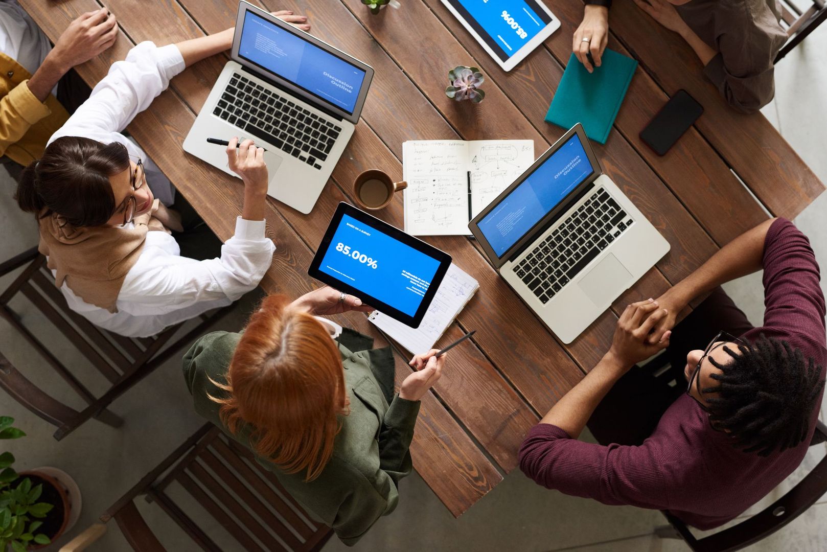 A creative team collaborating around a wooden table with laptops and tablets.