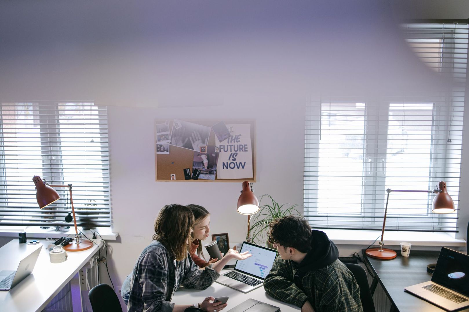 Team of creative designers collaborating over a laptop in a bright art studio office.