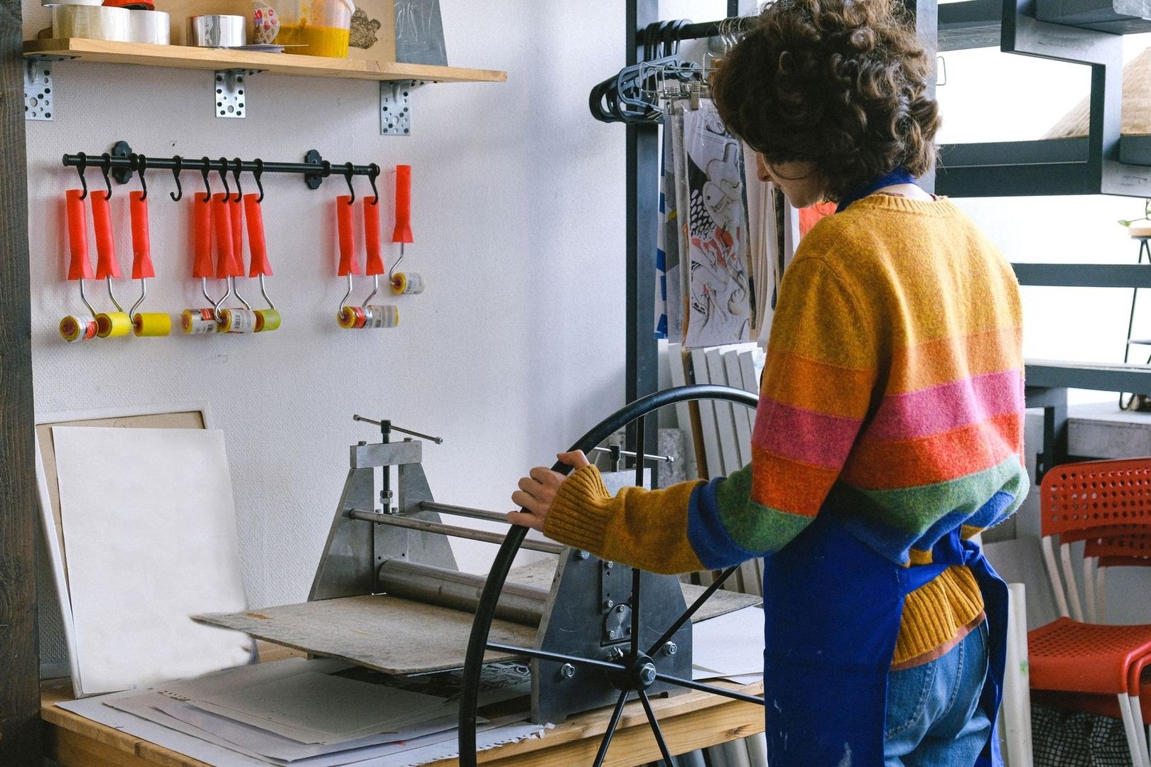 Artist operating a printmaking press beside hanging brayers