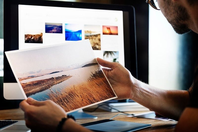 Person compares a printed landscape photograph with images on a computer