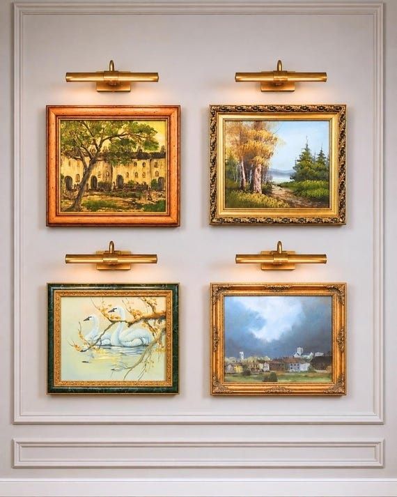 Four framed landscape paintings illuminated by brass picture lights