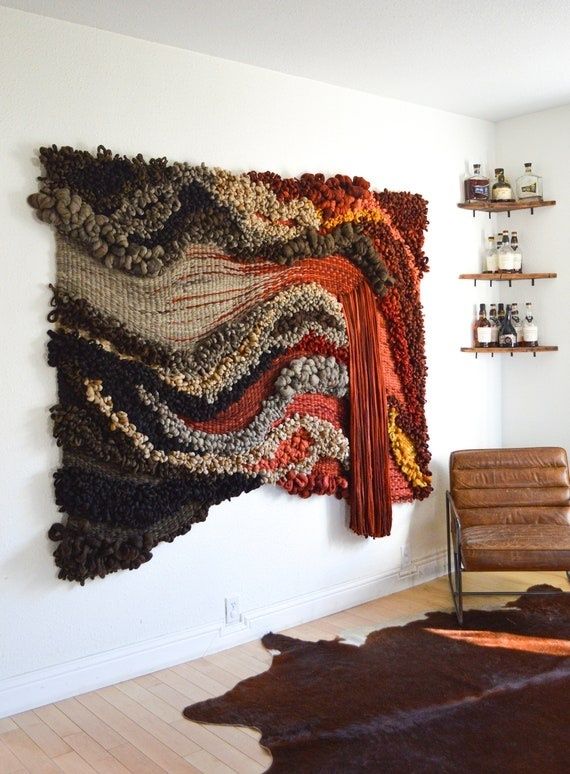 Dimensional woven fiber wall hanging beside shelves and a leather chair