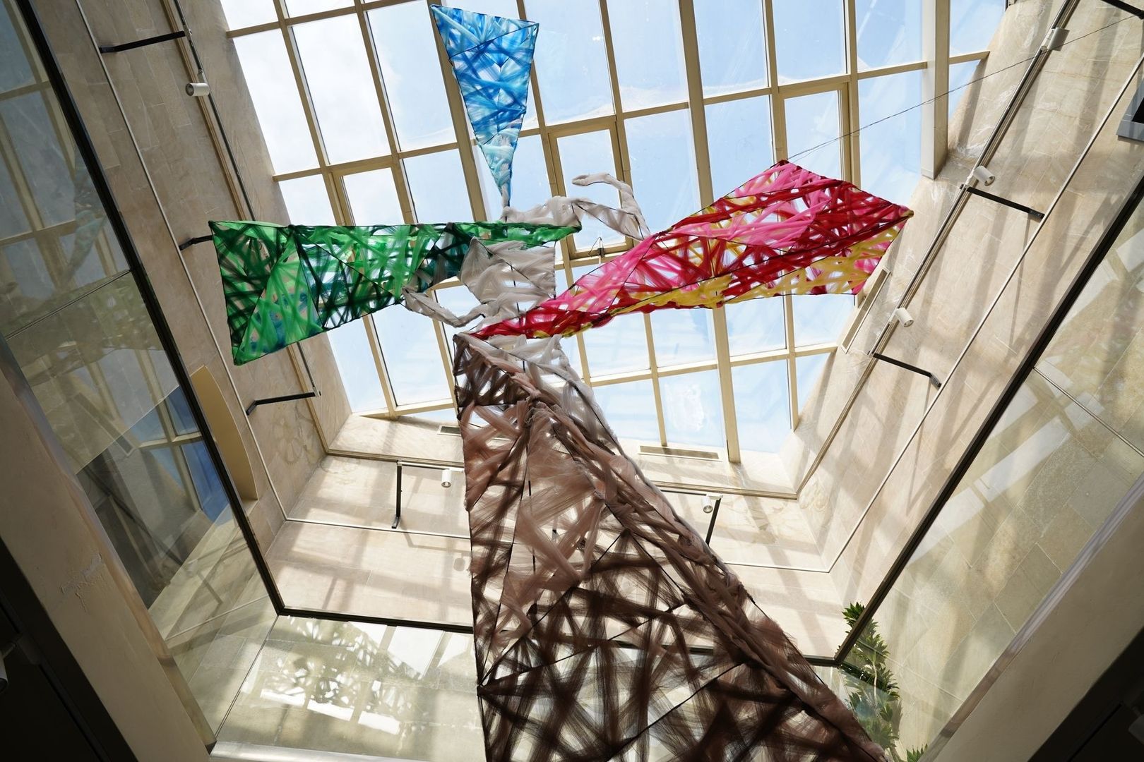Suspended colorful fiber sculpture beneath a glass atrium roof